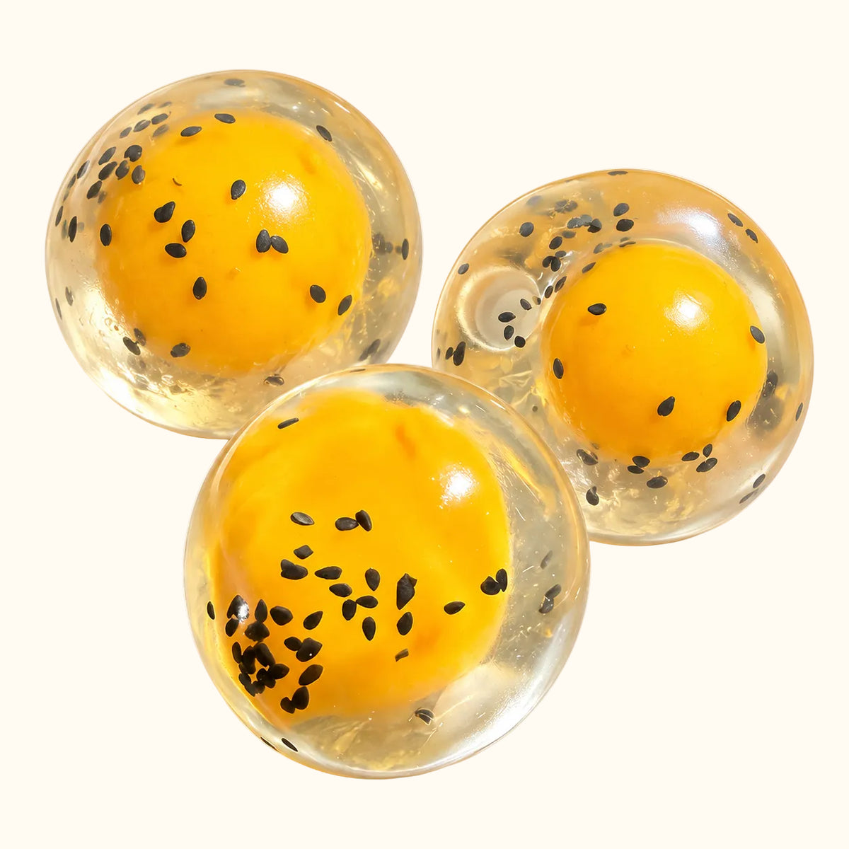 Three translucent SQUEEZU Crispy Egg Yolk Pastry Squishy Balls with yellow centers and black sesame-style details.