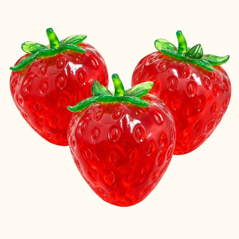 Three translucent red SQUEEZU Strawberry Squishy toys with leafy green tops and sculpted seeds.